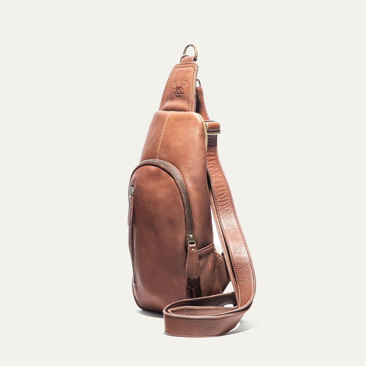 The WILL LEATHER GOODS - Zip Around Sling Bag in Cognac, featuring full-grain leather, a front zipper pocket, adjustable strap, and top handle, is shown upright against a plain light background.