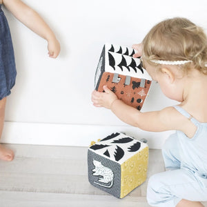 The WEE GALLERY - JUNGLE SOFT BLOCK by WEE GALLERY is a soft fabric cube perfect for stimulating a baby's developing senses. It features monochrome patterns and playful designs, including a cute monkey illustration on one side and a yellow leaf on another. Inspired by jungle life and animals, this toy boasts various textures and small loops on top for easy grasping.
