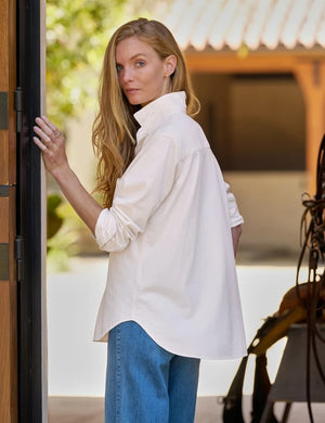 A person wearing the FRANK & EILEEN Waverly Button Up Tee in Vintage Jersey Vintage White, featuring a small label near the hem, paired with blue jeans and one hand tucked into a pocket.