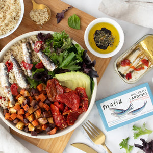 A rectangular package of MATIZ ESPANA Matiz - Sardinillas with Piquillo Peppers in Spanish Olive Oil. The blue package showcases an illustration of three sardines and includes details such as "Wild caught in the Eastern Atlantic," "1 gram of Omega-3's per serving," and "NET WT: 85g (3 oz).