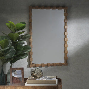 The ZODAX CADIER MANGO WOOD WALL MIRROR with a rectangular frame hangs on a textured gray wall above a wooden table displaying a potted plant, framed photo, books, and decor.
