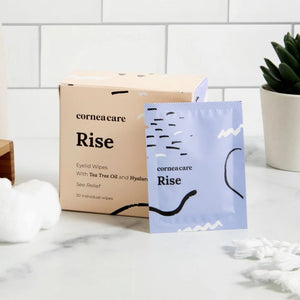 A CORNEA CARE packet, labeled "CORNEACARE - RISE EYELID WIPES," sits against a light blue backdrop with abstract wave and dot patterns. Infused with tea tree oil, it elegantly alleviates eye dryness.