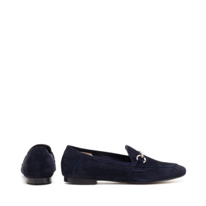 The MICHELE LOPRIORE - LEYLA LOAFER is a navy blue suede loafer adorned with a silver horsebit ornament on the vamp. Made in Italy and crafted from genuine leather, this shoe features a low heel and boasts a sleek, streamlined silhouette against a plain, off-white textured surface.