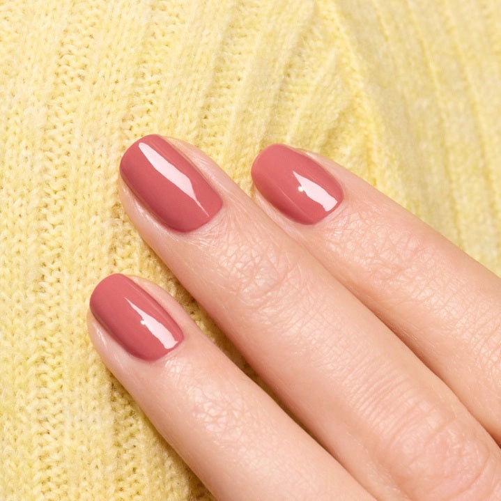 A close-up of a brush applying the smooth, glossy MANUCURIST - GREEN™ NAIL POLISH IN ROSEWOOD by MANUCURIST INC in a dusty pink rosewood shade on a flat surface, creating gentle curved lines in the polish.