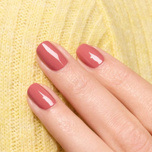 A close-up of a brush applying the smooth, glossy MANUCURIST - GREEN™ NAIL POLISH IN ROSEWOOD by MANUCURIST INC in a dusty pink rosewood shade on a flat surface, creating gentle curved lines in the polish.
