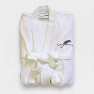 A folded white FEARRINGTON SIGNATURE COLLECTION - FEARRINGTON SPA ROBE from BOCA, with a belt tied in a knot, is displayed against a plain background. The kimono collar bathrobe features a black silhouette of a feather and "The Spa at Fairmont" embroidered on the chest.