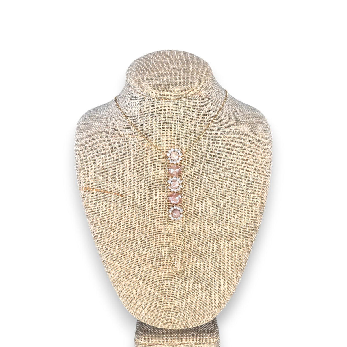 The GOLDISH - FLOWER PINK MOONSTONE AND WHITE PEAR LADDERS TO BLISS NECKLACE by GOLDISH features a vertical floral pendant with four pink moonstones and small clear stones, inspired by sacred geometry. Displayed on a beige fabric bust.