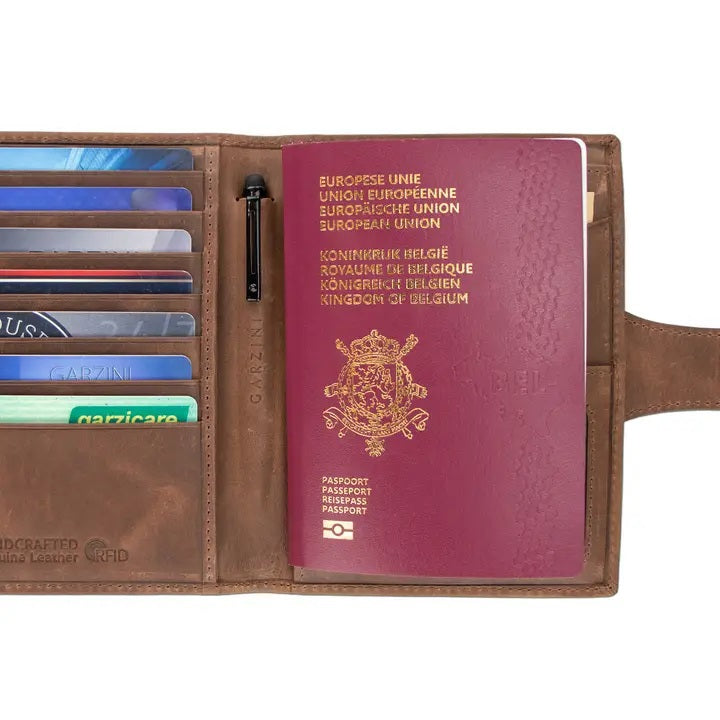 GARZINI RFID-blocking leather passport holder with AirTag compartment in brown, featuring a strap and snap button closure on a white background. The holder has a slightly worn, vintage look.