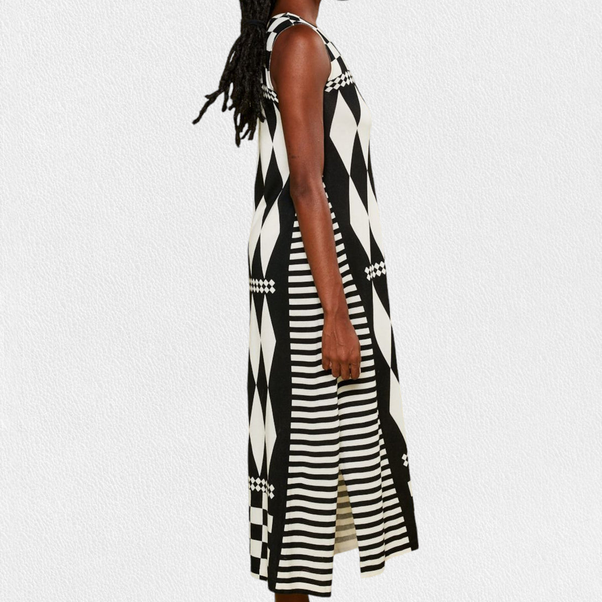 A person is wearing the IN BED WITH YOU - LONG KNIT DRESS featuring a sleeveless, knee-length design and a striking geometric pattern. The dress, from the Italian brand IN BED WITH YOU by CLAUDIOLAI SRL, showcases alternating squares and circles in vibrant prints of red, yellow, purple, and white set against a plain white textured background.