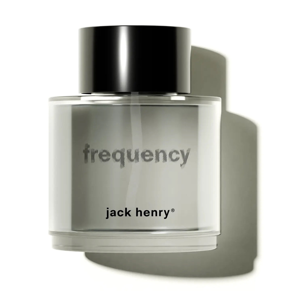 A clear glass bottle of JACK HENRY - FREQUENCY EAU DE PARFUM, with "frequency" and "JACK HENRY" labels and a black cap, sits on white, casting a soft shadow—an elegant, cruelty-free unisex fragrance by JACK HENRY.