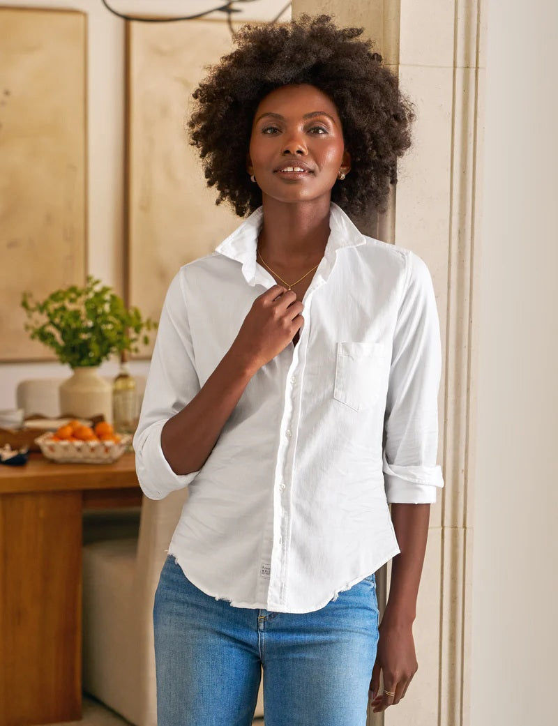 The FRANK &amp; EILEEN Barry Tailored Button Up in Famous Denim White features long rolled sleeves, a single chest pocket, and a curved hem, shown against a textured white background.