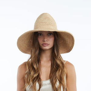 The WYETH HATS - LINA Raffia Sun Hat in Natural by WYETH features a packable, ultra wide brim and rounded crown, shown against a plain white background.