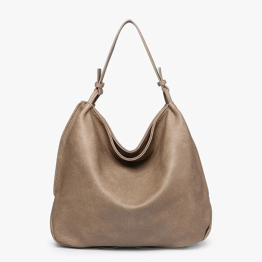 The JEN &amp; CO RUSTIC TOTE is crafted from brown vegan leather and features a relaxed, slouchy shape. Its simple and elegant design includes a single strap attached at both sides, along with an inner compartment for added functionality, all set against a plain light background.