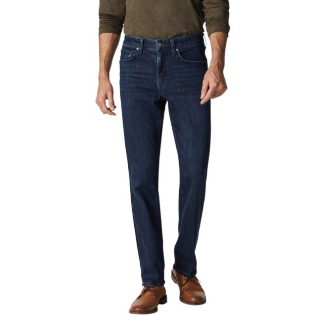 A man in a green long-sleeve shirt, brown shoes, and 34 HERITAGE Charisma Relaxed Straight Leg Jean in Dark Midnight Brushed Urban wash stands with his back to the camera against a plain white background.