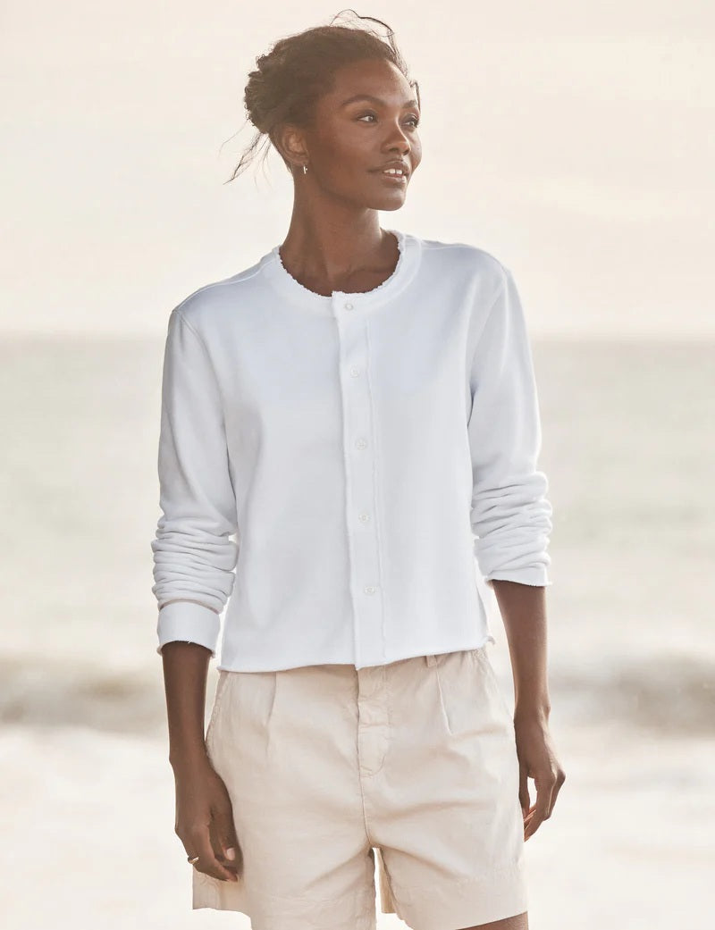 A woman stands on the beach in the FRANK &amp; EILEEN JACKIE Sweatshirt Cardigan in white, gazing sideways with the ocean and sky behind her.