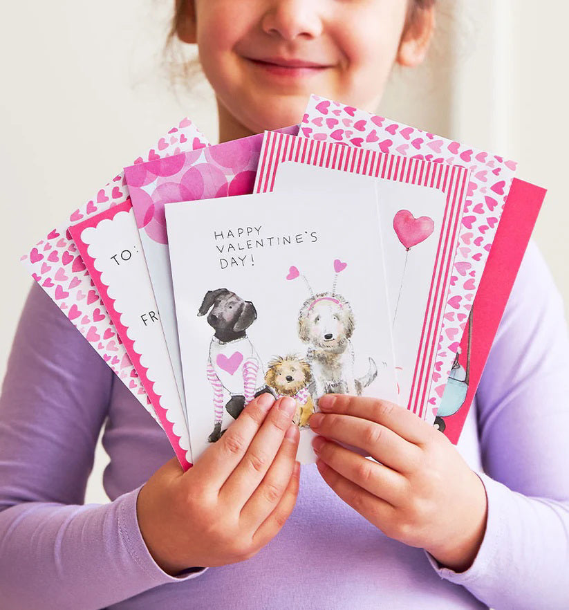 The E. FRANCES PAPER - DOGGIE DRESS-UP CLASSROOM VALENTINE SET features three dogs dressed festively: one in striped pajamas, another with a heart bandana, and a third with heart antennae. “Happy Valentine’s Day!” is displayed across the top against a backdrop of pink hearts, ideal for charming Valentines or envelopes.