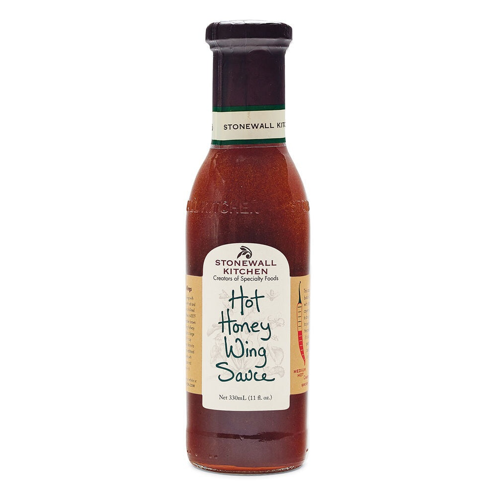 A bottle of STONEWALL KITCHEN - HOT HONEY WING SAUCE, featuring a beige label with green accents and standing upright on a white background, offers the perfect balance of sweet heat for anyone who enjoys a spicy wing sauce.