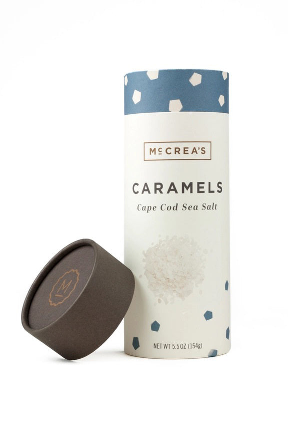 A cylindrical container of McCREA'S CANDIES Cape Cod Sea Salt Caramels features a blue and white geometric lid, the brand name, and a sea salt illustration, inspired by New England.