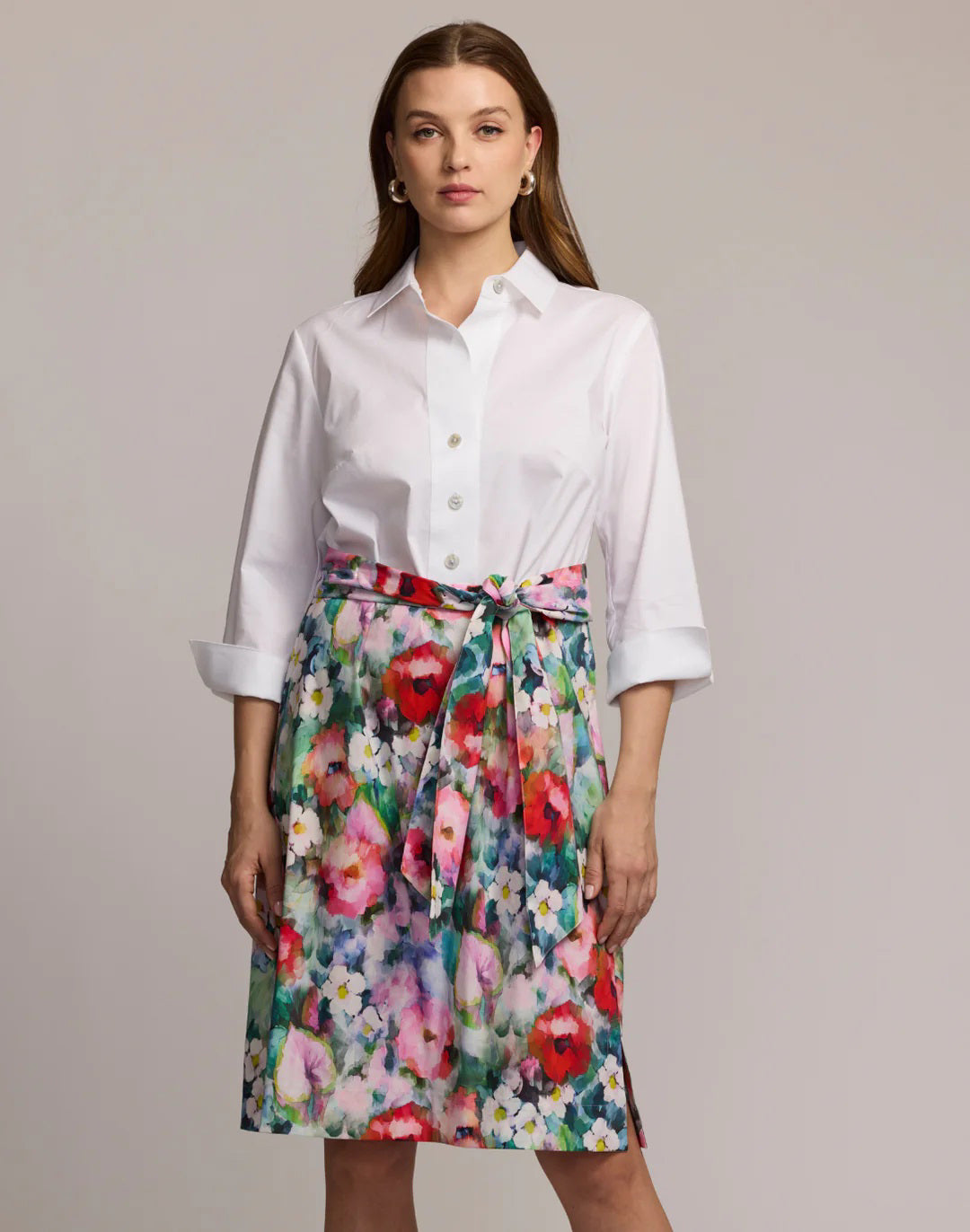 A woman faces forward in the HINSON WU CHARLOTTE 3/4 Sleeve Watercolor Garden Combo Dress, featuring a premium cotton-blend white button-up top and a colorful floral skirt with a matching tied belt. The background is plain and neutral.