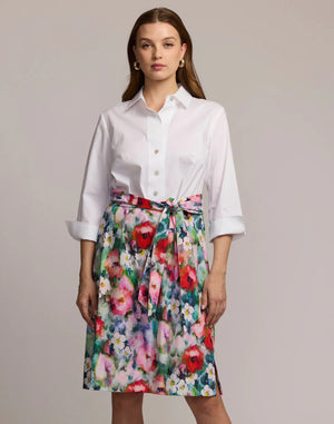 A woman faces forward in the HINSON WU CHARLOTTE 3/4 Sleeve Watercolor Garden Combo Dress, featuring a premium cotton-blend white button-up top and a colorful floral skirt with a matching tied belt. The background is plain and neutral.