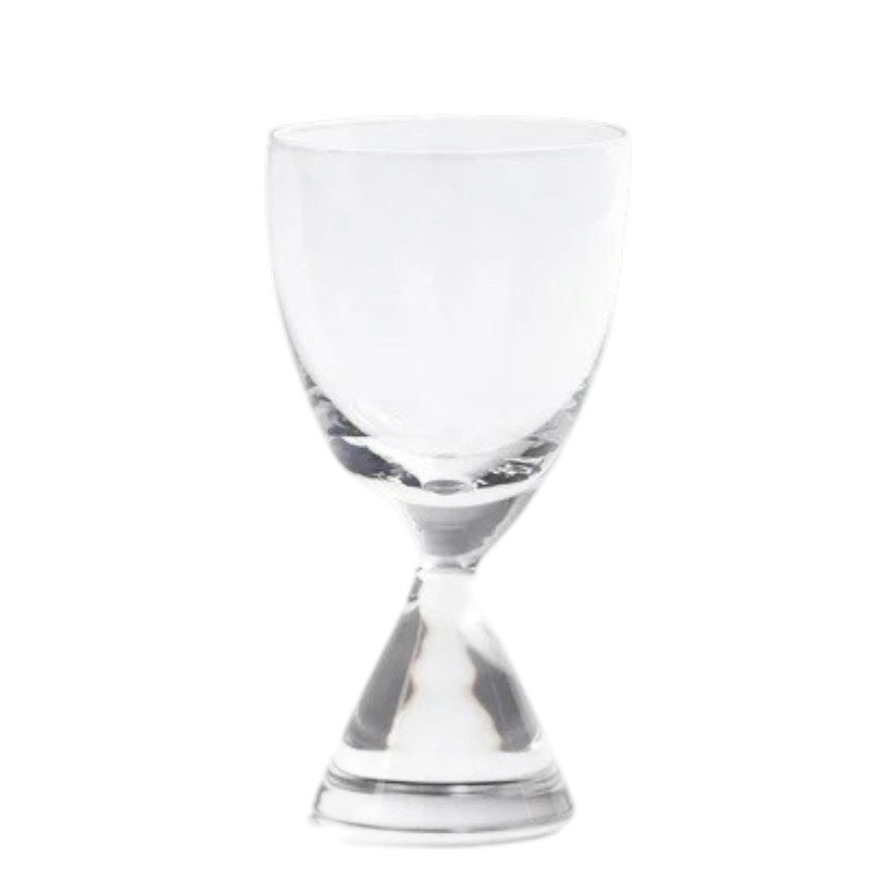 The ZODAX TIMELESS SIP SHOT GLASS, featuring a unique double-ended shape, sits half-filled with amber liquid on a light surface, while two dark round dishes are softly blurred in the background.