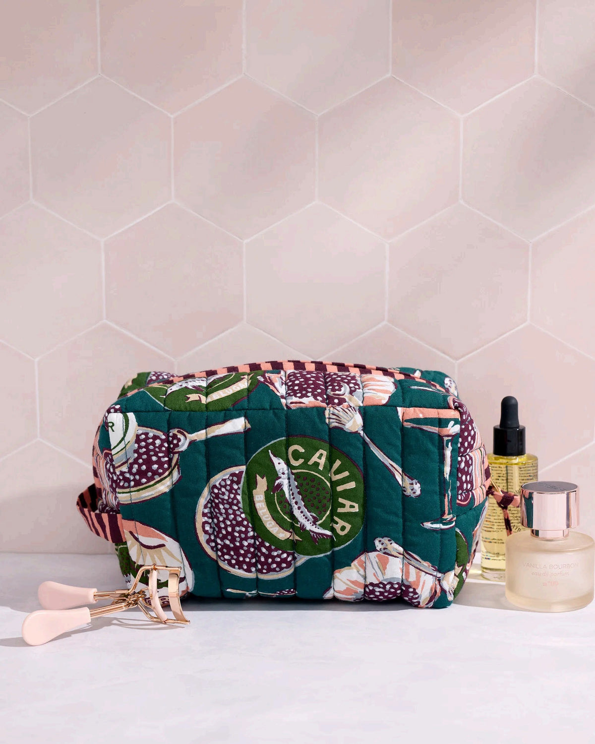Adorned with an illustrated pattern of caviar tins, open shells brimming with caviar, delicate spoons, and tall champagne glasses on a rich peacock feather green background, the PRINTFRESH - CHAMPAGNE & CAVIAR QUILTED POUCH IN PEACOCK FEATHER is an elegant accessory from PRINTFRESH. This stylish pouch makes a perfect gift for her.