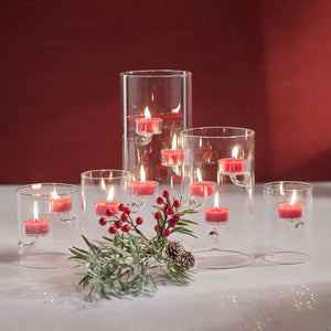 Five ZODAX SUSPENDED GLASS TEALIGHT HOLDER - EXTRA LARGE candle holders with floating tealights are arranged on a gray surface, with driftwood in the background. The windproof holders vary in height for an elegant display.