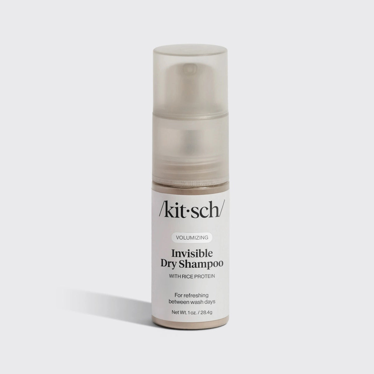 A bottle of KITSCH Volumizing Invisible Rice Protein Dry Shampoo stands upright on a light background. This non-aerosol, mess-free formula by KITSCH refreshes your hair with rice protein and comes with a clear cap and white label.