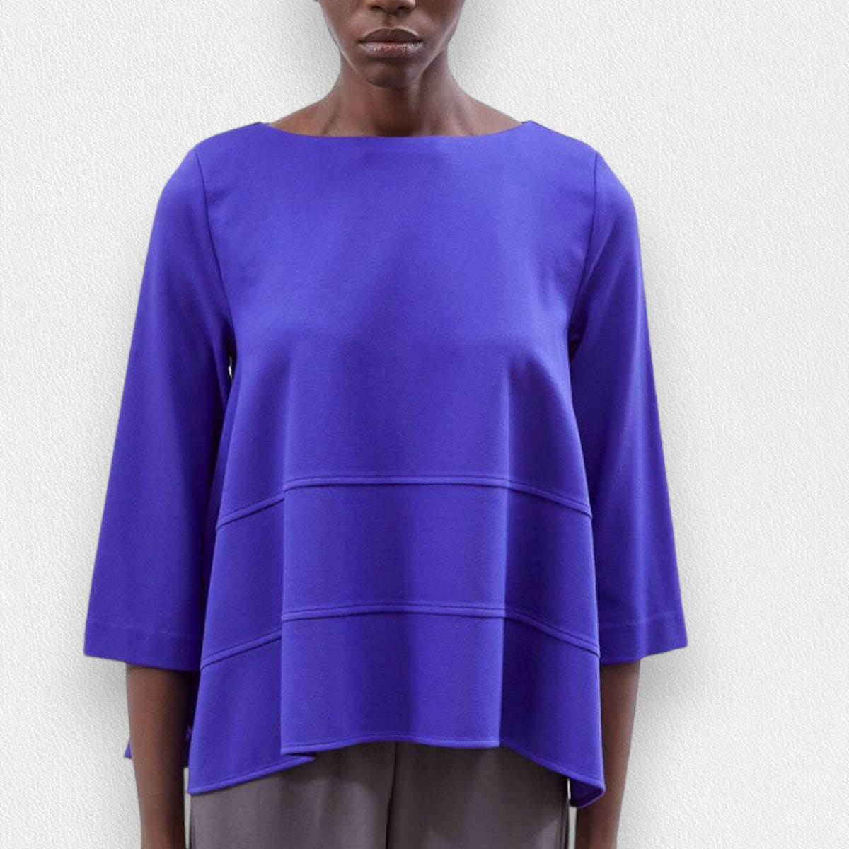 A person is wearing the MEIMEIJ - OVERSIZED CREW NECK TOP by MEIMEIJ, featuring a loose-fitting, long-sleeve design in royal blue with horizontal seam details across the front. Made in Italy, this top has a round neckline and slightly flares out at the bottom. Only the upper torso is visible against a plain, off-white background.