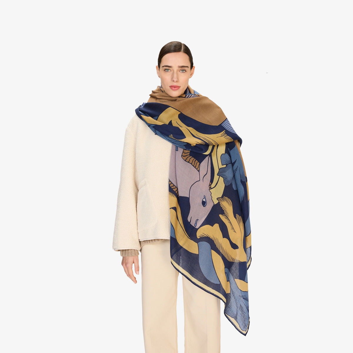 The INOUI CAVALE HORSE WOOL SCARF in navy features an abstract design with stylized tan and lavender rabbits among blue and yellow leafy shapes, all set against a dark blue background.