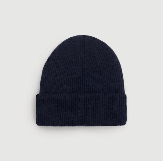 The HARTFORD - SEAMLESS WOOL BEANIE IN NAVY by HARTFORD is a dark blue ribbed knit beanie made from 100% wool, featuring a folded brim and shown against a plain light gray background.