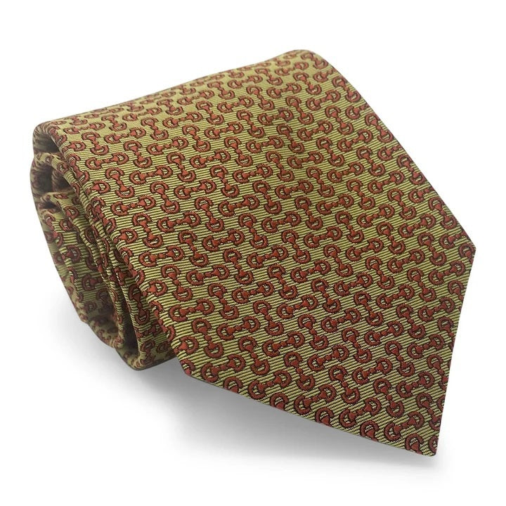 A close-up of the BIRD DOG BAY PETER-BLAIR - HORSEBIT SILK TIE IN YELLOW, featuring a handmade New York woven silk construction with a repeating pattern of small red horseshoes and horse heads on a yellow background. The tie has a pointed tip at the bottom.