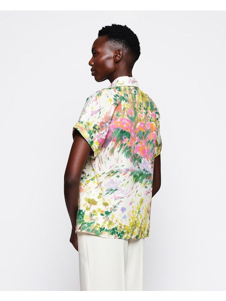 Against a plain white background, someone with short hair wears light-colored pants and the vibrant MIRTO 1956 - Brushstroke Print Cotton Shirt, showcasing its colorful floral and brushstroke design.