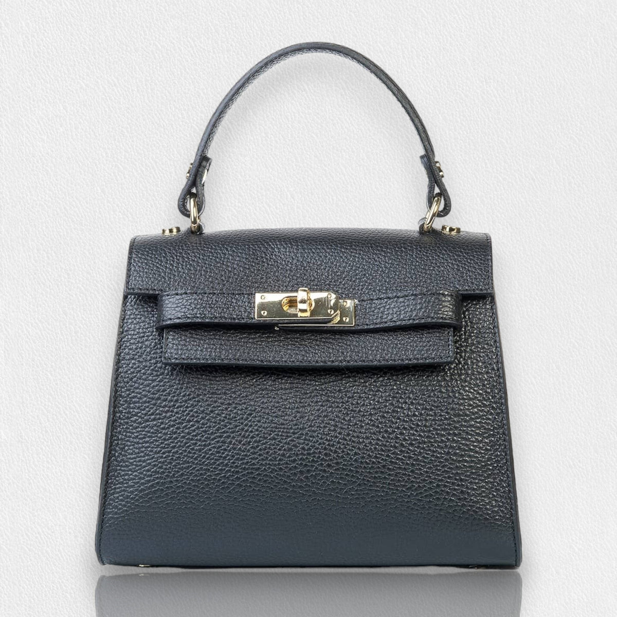 The LE BORSETTE LEATHER SATCHEL BAG is a small, structured satchel-shaped handbag in light pink, featuring a gold clasp at the front. It boasts a single top handle, an adjustable shoulder strap, and two gold-tone hardware pieces on either side of the handle. The textured leather adds to its luxurious and elegant appearance against the plain white background.