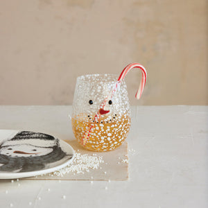 The CREATIVE COOP CONFETTI DRINKING GLASS WITH SNOWMAN FACE is a clear, stemless glass with a textured, bubbly surface and a cheerful snowman face featuring black dot eyes and mouth plus an orange-red curved nose.
