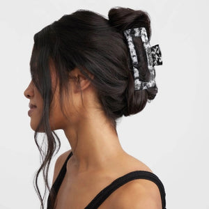 The KITSCH - Eco Friendly Jumbo Open Shape Claw Clip in Black is a rectangular hair accessory featuring a marbled black and white pattern, cutout center, and curved edges. Made from recycled materials, it is displayed on a light gray background.