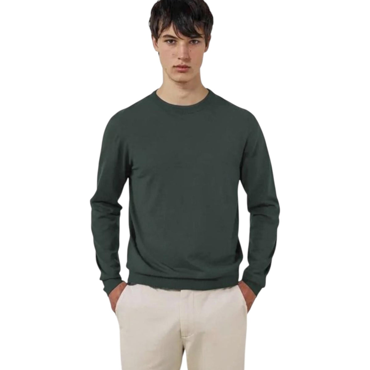 A young man stands with his hands in his pockets against a white background, wearing the HARTFORD Extra-Fine Merino Wool Crew Pullover in Forest and light-colored pants.