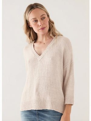 A woman with light hair wears the BASE MILANO V NECK COTTON SWEATER in light beige, styled with blue jeans, against a simple light background.