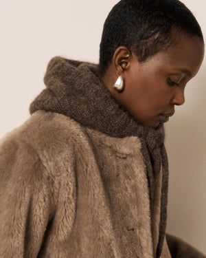 Wearing the HARTFORD MEVA Hood in Chocolate, a person gazes seriously at the camera against a plain background.
