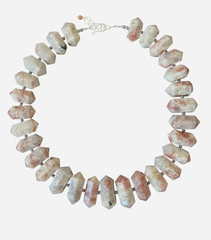 The ANN LIGHTFOOT RAS DU COU OF DOUBLE POINTED SUNSTONE necklace features large, double-pointed sunstone beads in white, gray, and reddish hues with small dark spacers on a white cord.