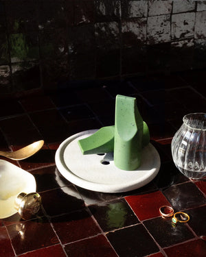 The UME - HERBES DE PROVENCE ERODE MINI SOAP by UME STUDIO is a green, smooth, abstract soap with a tall cylindrical base, slanted flat top, and curved cut on one side, shown against a light gray background.