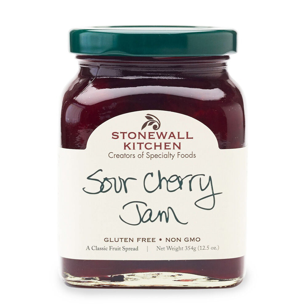 A glass jar with a green lid contains STONEWALL KITCHEN-SOUR CHERRY JAM, ideal for any cherry aficionado. The label displays "Stonewall Kitchen Creators of Specialty Foods" and "Sour Cherry Jam." Additionally, it indicates "Gluten Free" and "Non-GMO." Net weight is 354g (12.5 oz).