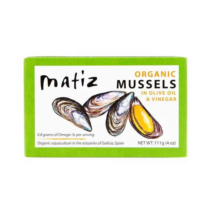 A green rectangular box labeled "MATIZ - MUSSELS IN ORGANIC OLIVE OIL" from MATIZ ESPANA. The box features illustrations of three mussels, one of which is open to show the yellow inside. It also notes "0.8 grams of Omega-3s per serving" and weighs 111g (4 oz).