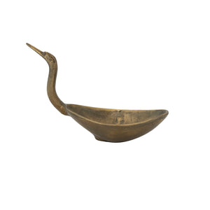 The CREATIVE COOP BIRD SHAPED BOWL IN ANTIQUE BRASS FINISH features an elongated neck and beak forming the handle, with the body as the bowl, creating a unique decorative accent.