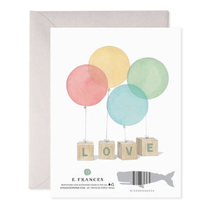 The E. FRANCES PAPER BABY BLOCKS GREETING CARD features four colorful balloons in red, yellow, green, and blue tied to wooden blocks spelling "BABY." This handcrafted card, made in the USA, comes with a plain envelope.