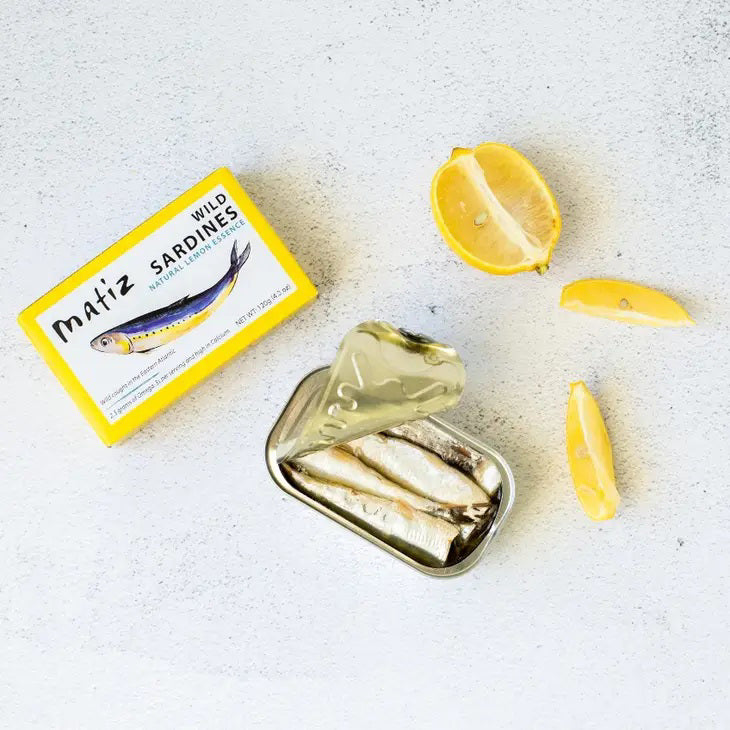 MATIZ ESPANA's MATIZ - SARDINES WITH LEMON comes in a yellow box featuring a sardine illustration. Key highlights include "Wild caught in the Eastern Atlantic," "2.3 grams of Omega-3s," "High in Calcium," and "Rich flavor." Contains 120g (4.2 oz); includes Spanish olive oil and lemon essence.