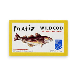 A yellow tin labeled “MATIZ - WILD COD IN SPANISH OLIVE OIL” from the brand MATIZ ESPANA showcases an illustration of a cod fish and the blue MSC certified logo, signifying sustainable sourcing. The net weight is 111g (4 oz), and text highlights that the salt-cured cod is caught in the Eastern Atlantic.