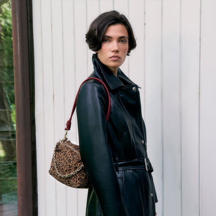 The CRAIE STUDIO - MINI HALO LEO SEPIA BAG by CRAIE STUDIO is a striking leopard-print suede leather handbag, showcasing a silver chain and vivid red leather shoulder strap, beautifully presented against a white background.