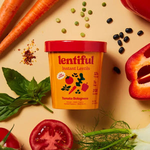 A container of LENTIFUL - LOW SODIUM TOMATO BOLOGNESE INSTANT LENTILS by LENTIFUL is surrounded by fresh carrots, spinach, tomatoes, bell pepper, beans, peas, herbs, and red pepper flakes for a heart-healthy meal.