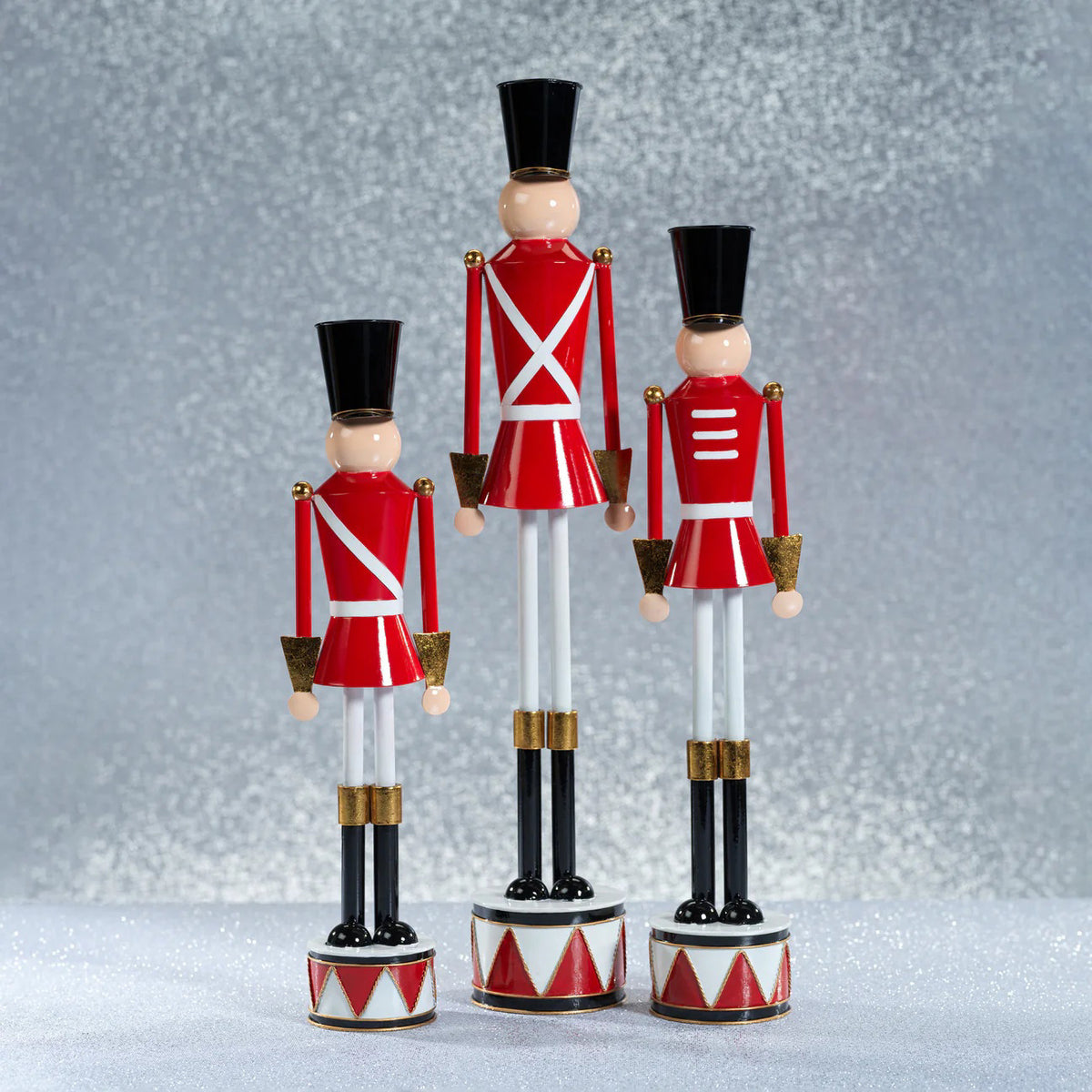 The ZODAX ALLOY FESTIVE DECORATIVE SOLDIER - TALL features a classic nutcracker style with alloy accents, a red coat, white straps, gold details, and stands upright on a small drum base for a modern festive touch.